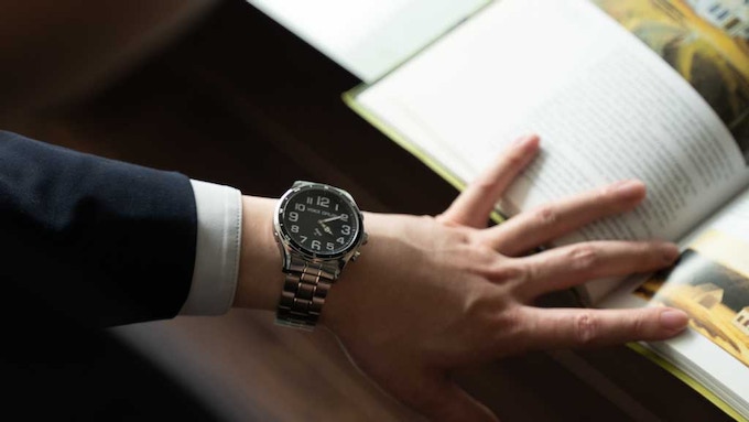 Picture of a businessman opening a book with his hand wearing a GNSS voice wristwatch.